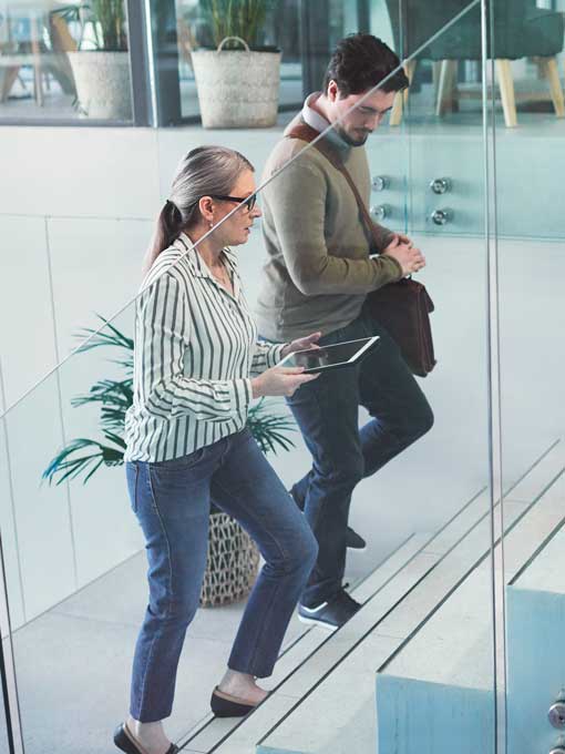Mature business woman in deep conversation with younger business man while walking up stairs in a modern office